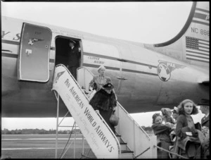 Mrs Hodges [dec?] wearing a short fur coat, walking down a gangway, on arrival of a PAA (Pan American Airways) Clipper Kathay NC88883 aircraft, location unidentified