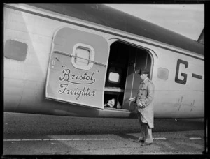 View of an unidentified [reporter?] in front of open side door waiting to interview crew off visiting Bristol Freighter transport plane 'Merchant Venturer' G-AIMC, Whenuapai Airfield, Auckland