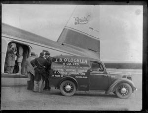 View of J B O'Loghlen's truck with unidentified people by an open side door of the Bristol Freighter transport plane 'Merchant Venturer' G-AIMC, Whenuapai Airfield, Auckland