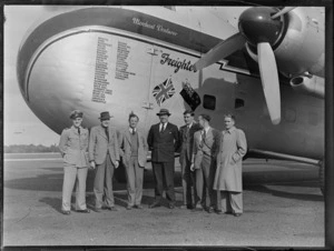 Group portrait of Mr N Higgs with crew members of the visiting Bristol Freighter transport plane 'Merchant Venturer' G-AIMC with names of airports visited on front cargo door, Whenuapai Airfield, Auckland