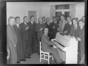 Group of unidentified men, standing and singing around a piano, while man plays, during an Auckland Aero Club dinner, Auckland