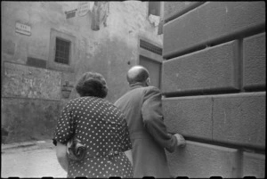 Italian civilians peer around corner of street crossed with enemy machine gun fire in Florence, World War II - Photograph taken by George Kaye