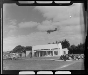 Rearwin Sportster aeroplane in flight over clubrooms at Auckland Aero Club, Mangere, Manukau City, Auckland Region