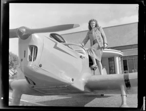 Miss Stormont standing on the wing of an aeroplane, outside Auckland Aero Club clubrooms, Mangere, Auckland