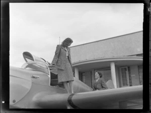 Miss Stormont, who is standing on the wing of an aircraft, talking to Mrs Exton, at Auckland Aero Club, Mangere, Auckland