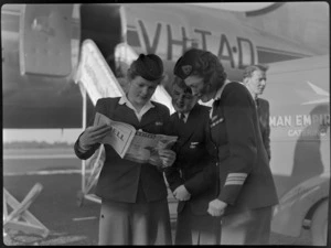Flight attendants - Miss L Armstrong (left) of TAA (Trans Australia Airlines), Miss P Woolley of TEA (Tasman Empire Airways) and Miss M Harrison of TAA, reading Whites magazine, standing in front of TEA van, including aircraft VH-TAD McDouall Stuart in the background, unidentified location