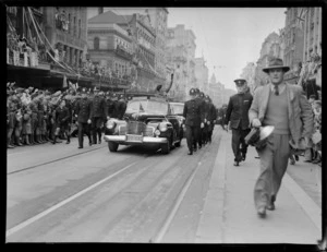 Lord Montgomery standing in car, waving to people in street parade, including policemen marching alongside vehicle, and Auckland Power Board building, [Queen Street?], Auckland