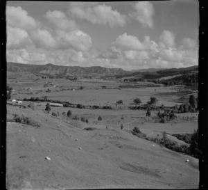 View down on a farmland valley with sheep, cattle, farm buildings, a river and road, with native forest covered hills beyond, Mahoenui district, Waikato Region