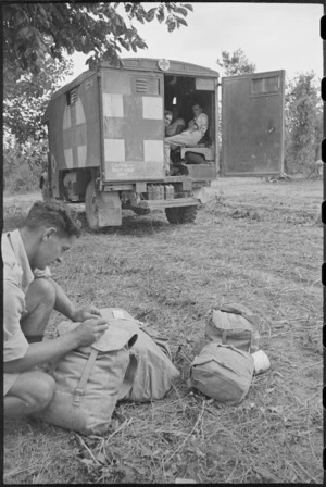R Aiken at advanced dressing station of 4 NZ Field Ambulance writing personal details on kits, Italy, World War II - Photograph taken by George Kaye