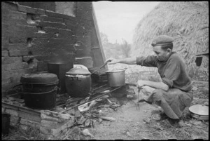 D Charlewood, a cook of 22 NZ Battalion stokes up his fire in forward areas near Rimini, Italy, during World War II - Photograph taken by George Kaye