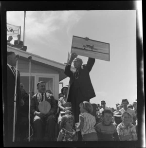 Official holding poster of aeroplane with crowd at Whakatane Airport opening