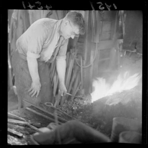 Unidentified blacksmith heating metal object in a forge at a workshop, Johnsonville, Wellington