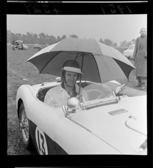 Unidentified motor racing competitor, holding an umbrella and sitting in a racecar, Levin, Southern Manawatu