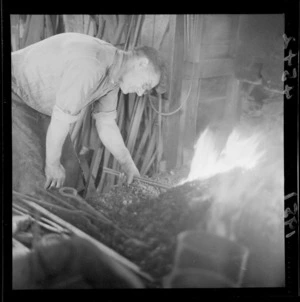 Unidentified blacksmith heating metal in a forge, in a workshop, Johnsonville, Wellington