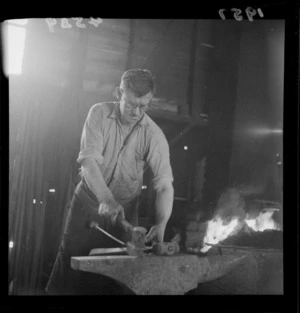 Unidentified blacksmith hammering metal on an anvil, with forge in background, Johnsonville, Wellington