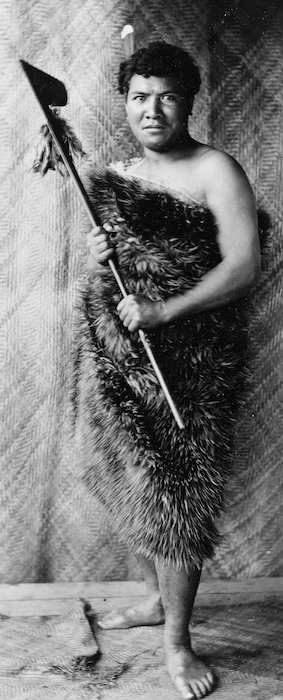 Unidentified Maori man wearing a kiwi feather cloak and holding a tewhatewha