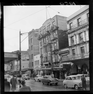 Scene on Willis Street, Wellington, including cars, pedestrians, ANZ Bank building, and businesses such as Sherwood's Jewellers, British Typewriters Limited, Ashley Aubery Limited, Nimmos, Shand-Miller School of Music, Sportswear Models Limited, and Tudor Cinema (which is showing film 'Suicide Batallion')