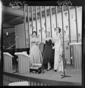 Models Mavis Watson, Glennis Cope, and Stephanie Anderson, wearing dresses at fashion show by Vogue Gowns (Willis Street) at Majestic Caberet, Wellington, including piano accordian