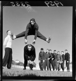 Australian boxers at a training session at Basin Reserve sportsfield, showing an unidentified man doing a frogleap over another man, observed by queue of team members and coach, probably Wellington