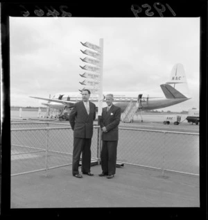 Mayor of Wellington, Frank Kitts, with an unidentified man, at [Whenuapai?] airport, Auckland, after arrival of first commercial flight from new Wellington Airport, National Airways Corporation Vickers Viscount aeroplane on tarmac in background
