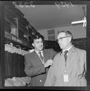 Ivan Vodanovich, Wellington rugby representative, assists an unidentified man who is trying on a jacket in a men's clothing store