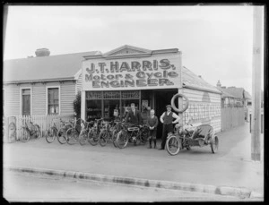 Group with bicycles and motorcycles outside the business of James Tasker Harris, motor and cycle engineer, on Sumner Road, Redcliffs, Christchurch