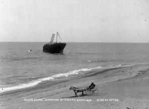 Timaru beach, showing the wreck of the ship Elginshire, and a man in a horse-drawn cart in the foreground