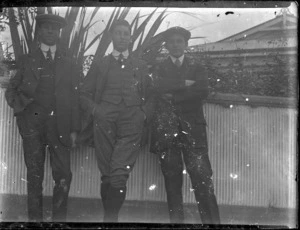 Three men in front of corrugated iron fence - taken by an unknown photographer
