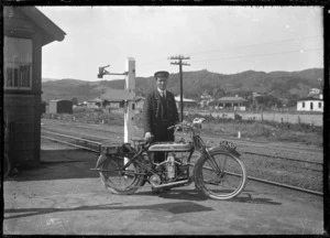 J McDonald standing beside a Douglas motorcycle, on the platform of the old Silverstream Railway Station, circa 1921.