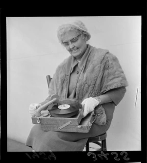 Portrait of Miss Joy Ridderhof holding a portable record player, location unknown, Wellington Region