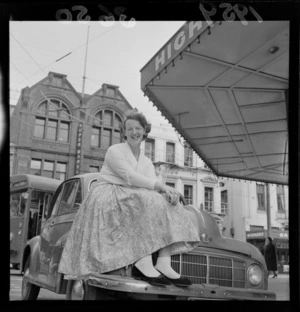 Miss D Masters, whose car was trapped at Wellington Airport, sitting on the bonnet of her Morris Minor motorcar, on Willis Street, Wellington
