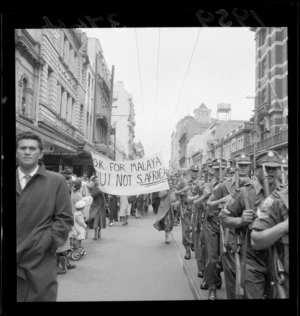 Crowd watching 2nd Battalion marching through Wellington street before leaving for Malaya, two women carry a banner reading 'OK for Malaya but not for S. Africa'