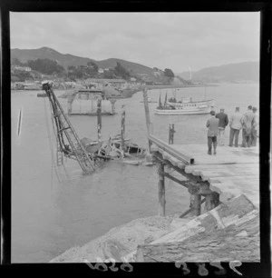 Crane in sea during Paremata Rail Bridge construction with unidentified men surveying the damage, Porirua District, North Wellington Region