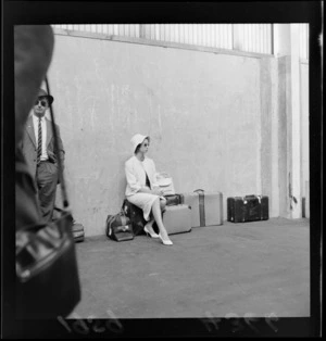 An unidentified smartly dressed female traveller, sitting in a suitcase at [ferry?] terminal, probably Wellington