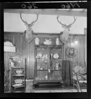 Interior view of a room at Riddiford Estate, showing stag heads on the wall and a china cabinet, Woburn, Lower Hutt