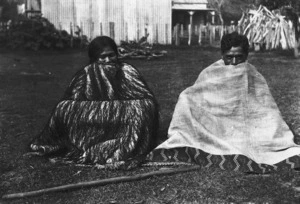 Rangihikatea Maihi and Maihi Wenetai, seated on grass and wrapped in cloaks (kakahu)