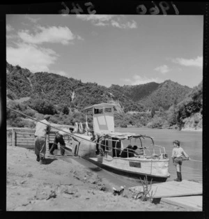 Men loading bales [to or from] river boat on the Whanganui River, with child watching on