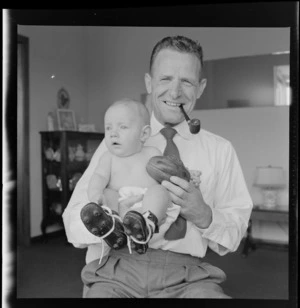 Neill McGregor holding miniature rugby ball and his baby grandson, Neill Thomas McGregor wearing small sized rugby boots