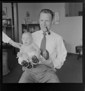 Neill McGregor holding miniature rugby ball and his baby grandson Neill Thomas McGregor wearing small sized rugby boots