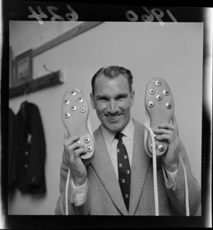 Wellington and NZ cricket batsman and bowler John Reid holding cricket boots within an unknown building, probably Wellington City