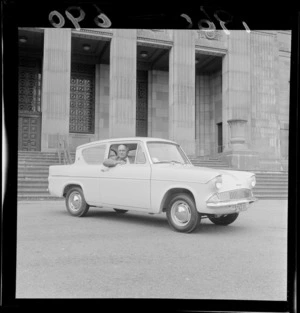A Ford Anglia car with Mr R B Gibbons at the wheel in front of the Dominion Museum, Buckle Street, Wellington City