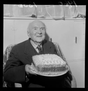 Portrait of Mr Edward Hughes on his 101st birthday holding his birthday cake within an unknown building location, probably Wellington Region