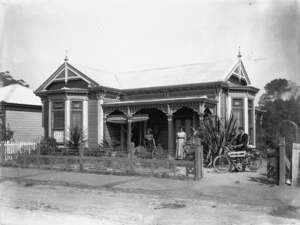 Two women and a man standing outside a house in Nelson with a bicycle and a motorcycle