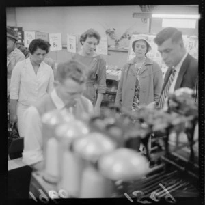 Shoppers watch a demonstration with a knitting machine with spools in foreground, James Smith Ltd, Manners Street, Wellington