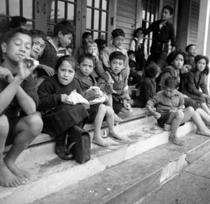 Children sitting on steps, in front of a school in Te Kaha, at lunch time
