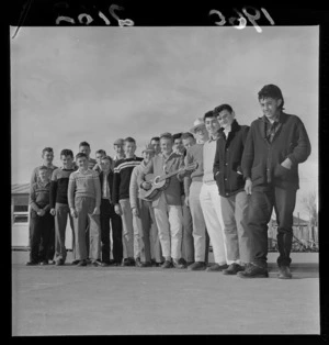 Group portrait of boys from Petone Technical Institute with a 'Johnny Devlin' named acoustic guitar in the courtyard, Petone, Wellington City