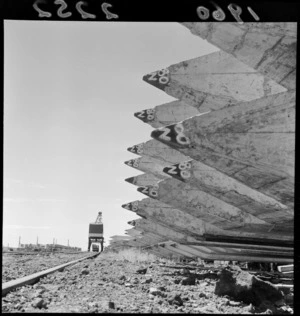 Wooden piles stacked to be used in wharf construction, with railway track alongside, Auckland