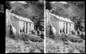 Unidentified men sitting outside of hut, unidentified location