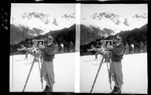 Unidentified photographer, with a camera, Mount Cook National Park, Canterbury Region, including skiers and spectators behind