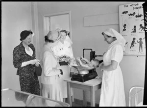 Queen Elizabeth II watches a baby being weighed at the Truby King-Harris (Karitane) Hospital, Dunedin
